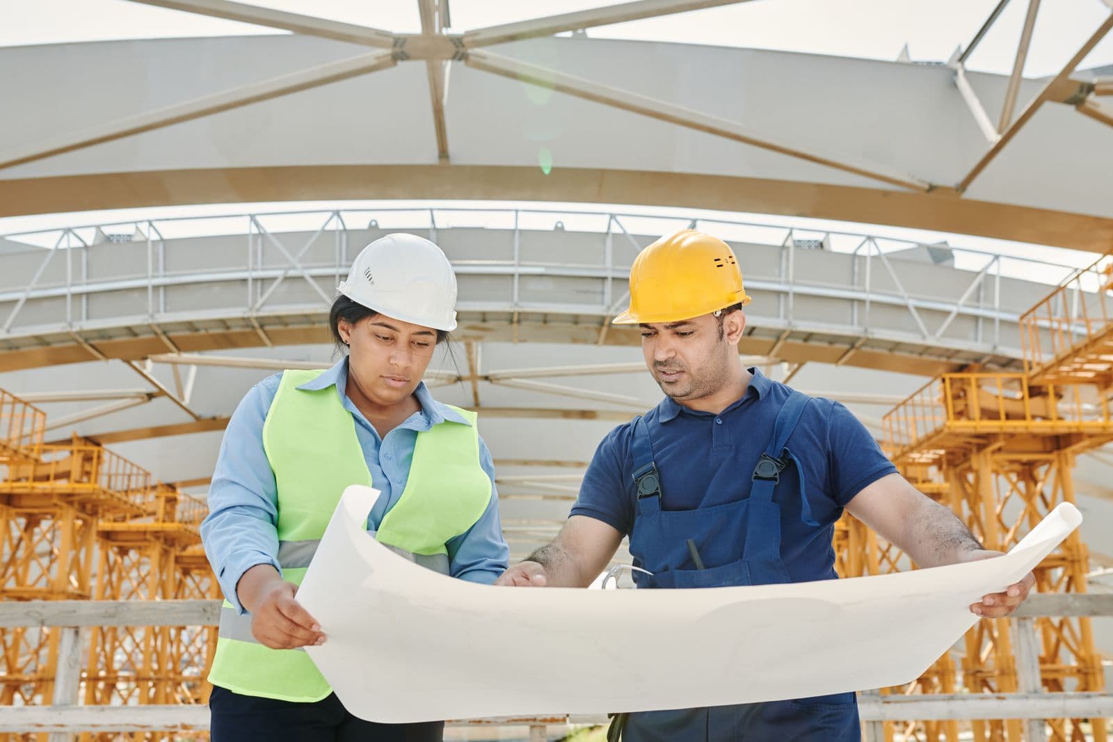 Dois profissionais com capacete analisando projeto em obra