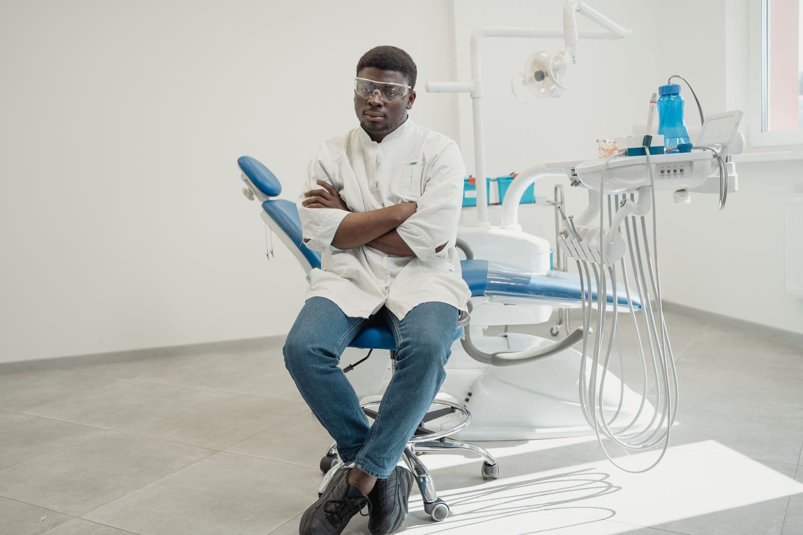 Dentista de jaleco branco sentado ao lado da cadeira odontológica