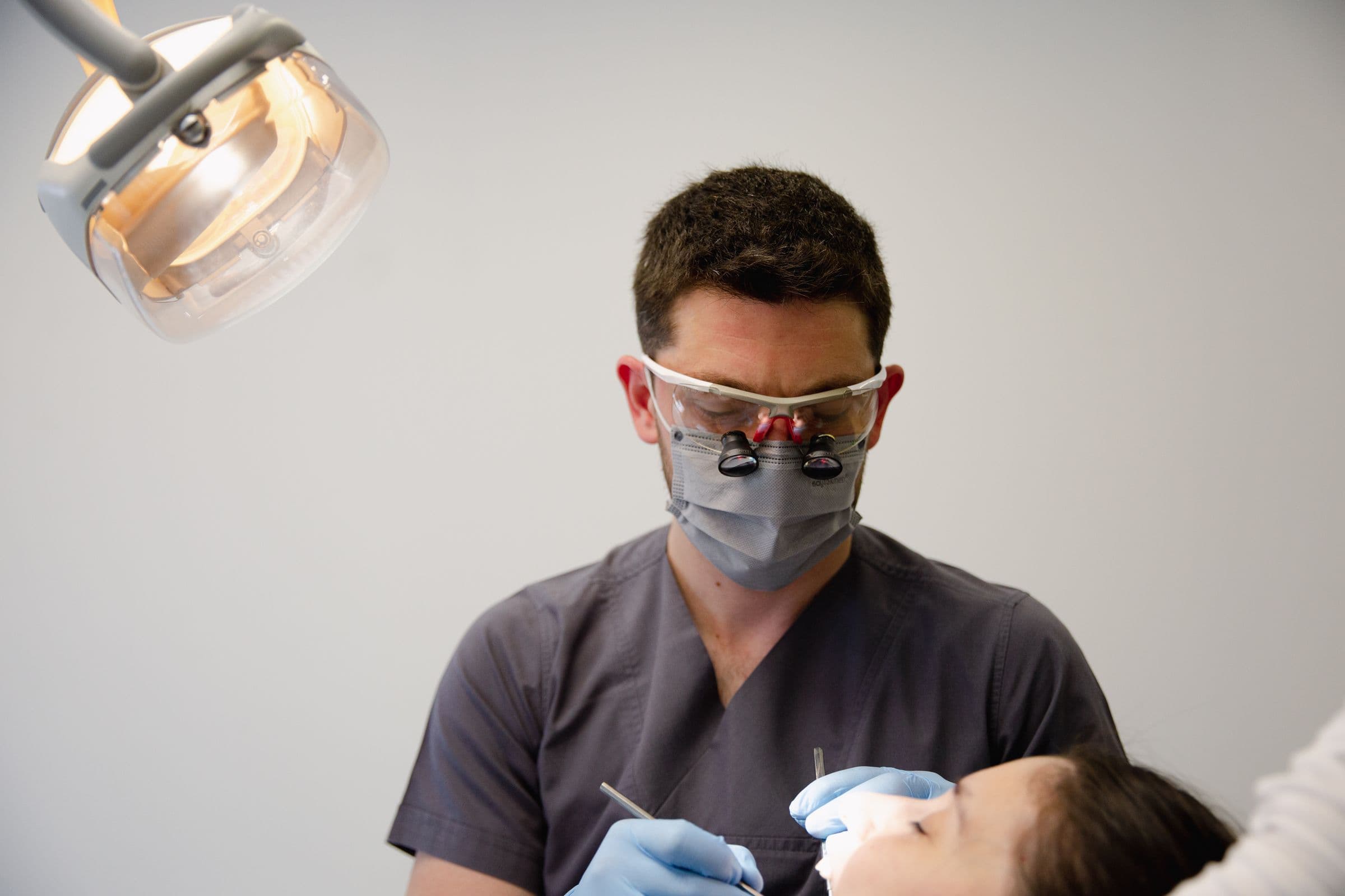 Dentista com lupas atendendo um paciente na cadeira