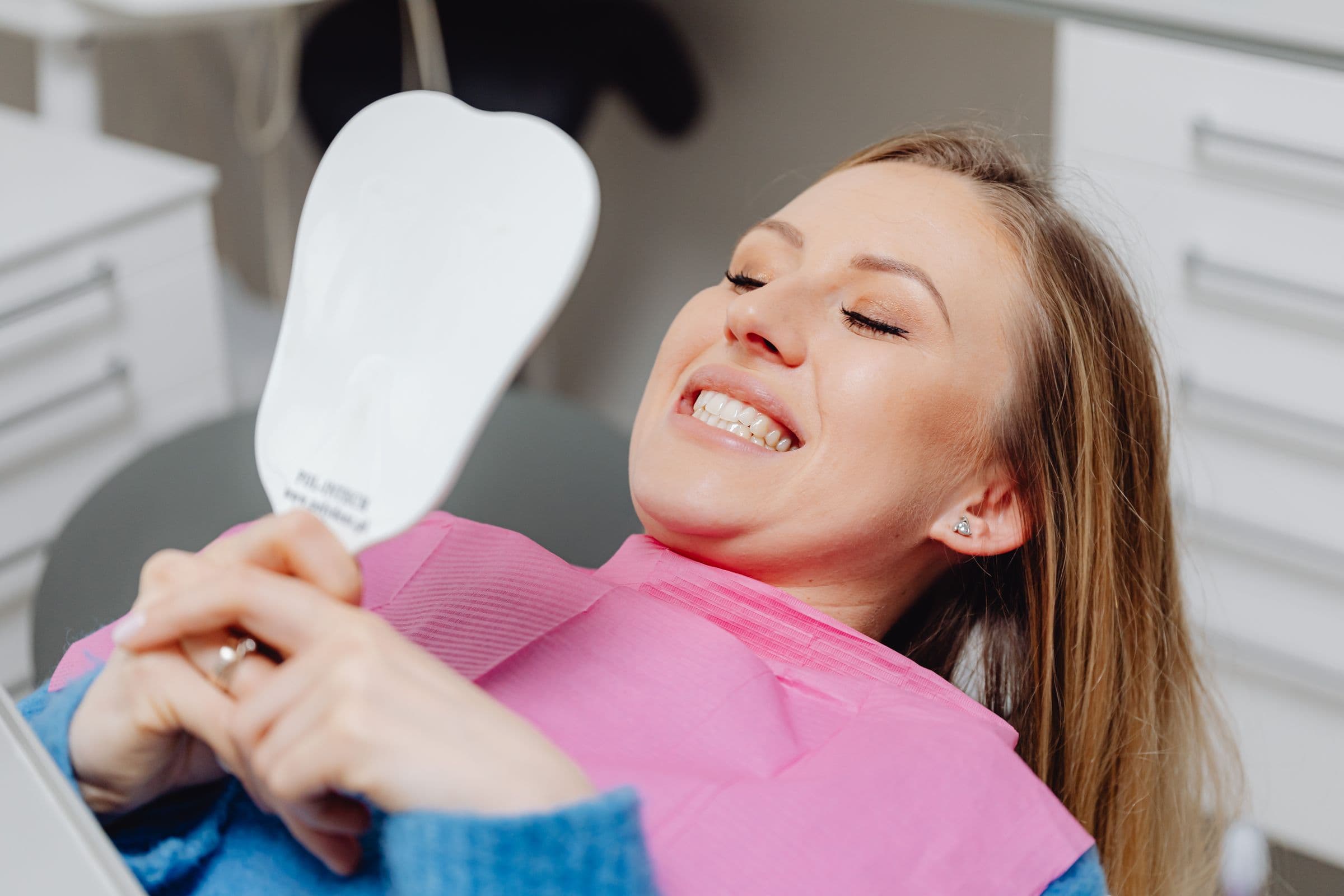Paciente na cadeira odontológica sorrindo ao ver os dentes no espelho